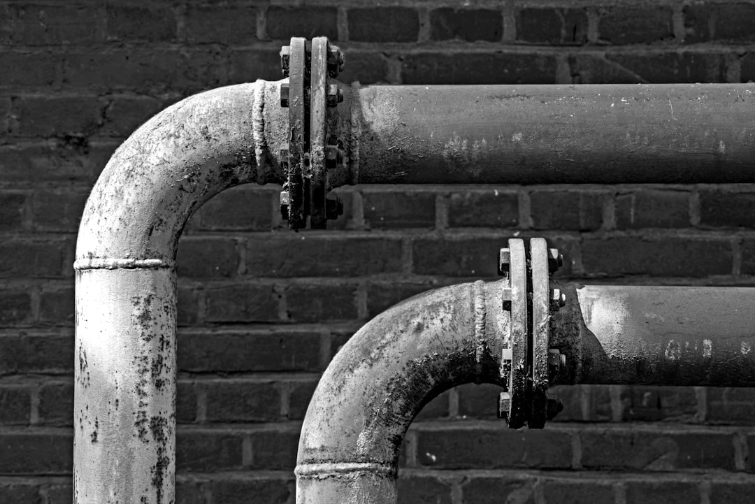 a-black-and-white-photo-of-pipes-on-a-brick-wall-cm-apc-od-w
