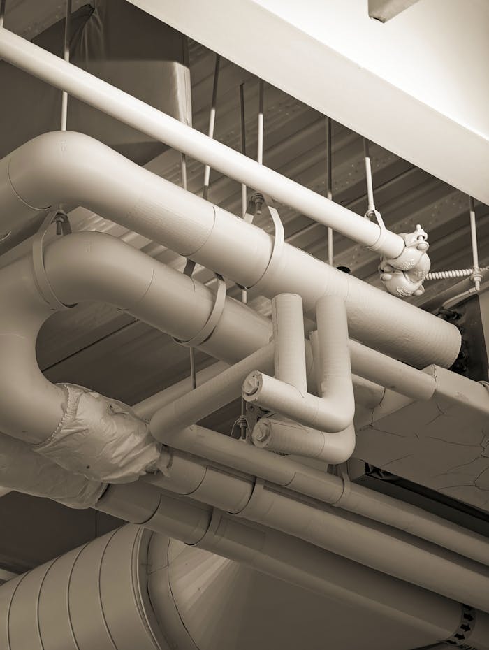 Complex network of industrial pipes and ducts in a sepia-toned indoor setting.