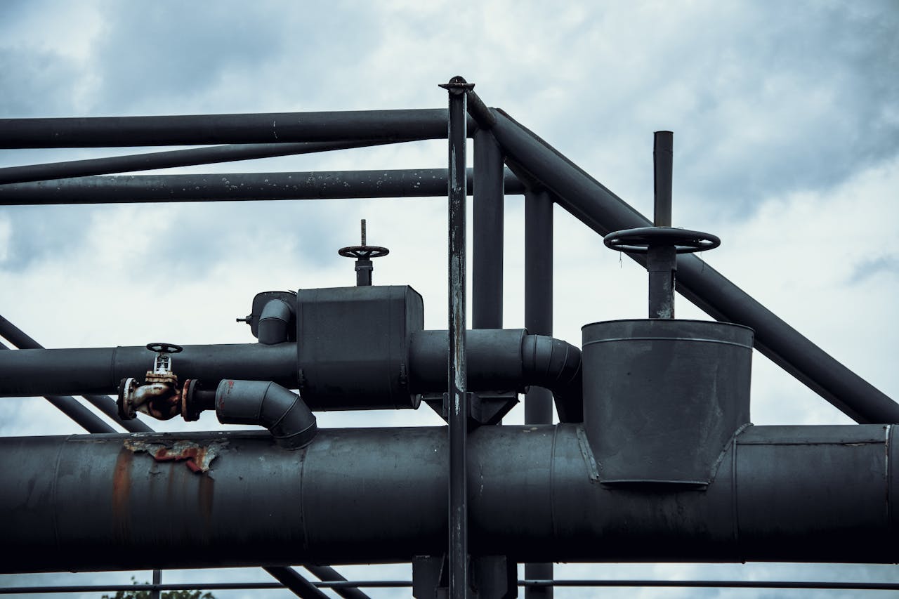 Close-up of industrial pipes and valves with rusty sections against a cloudy sky background.
